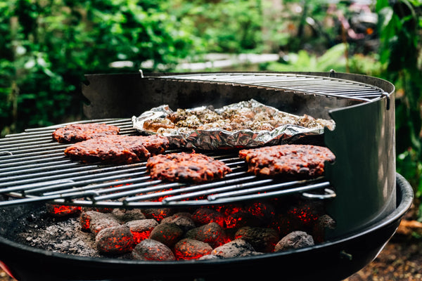 Grilled burgers and foil-wrapped veggies sizzling on a charcoal BBQ grill outdoors