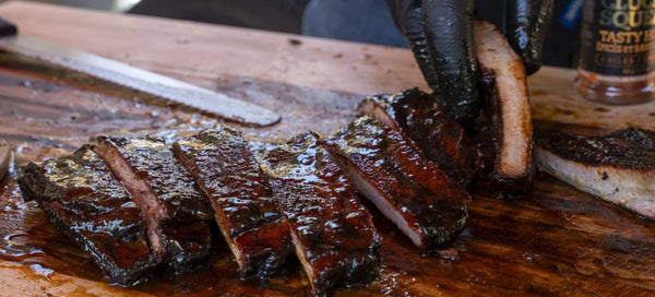 Juicy smoked ribs glazed with BBQ rub, sliced on wooden board, ready to serve